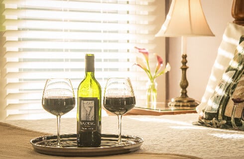 Bottle of white wine and glasses on a tray on a white-covered bed