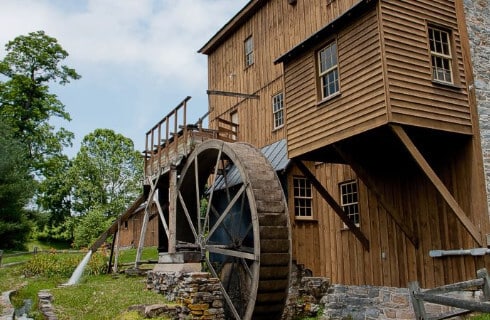 Wooden mill with large wheel next to a stream
