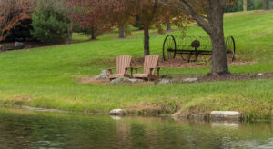 Front view of adirondack chairs sitting by a pond on the grass