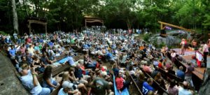 Hundreds of people seated on wood benches, attending a concert in "The Bowl" at Lime Kiln Theater in Lexington VA 