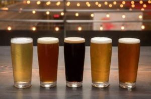 5 glasses of beer lined up on a table with string lights in the background