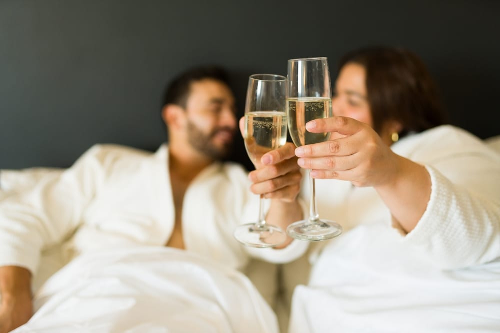 Couple toasting each other in bed with champagne during their romantic getaways in VA